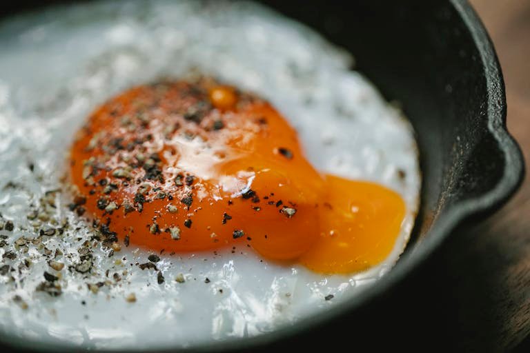 A delicious close-up of a fried egg with pepper seasoning, served in a black skillet.