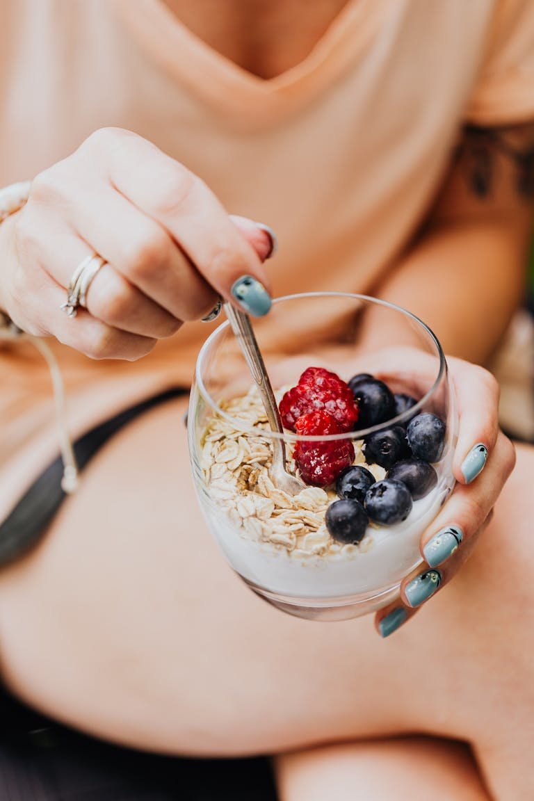 Close-up of a woman's hand holding a glass of yogurt with oats and fresh berries, a nutritious breakfast option.